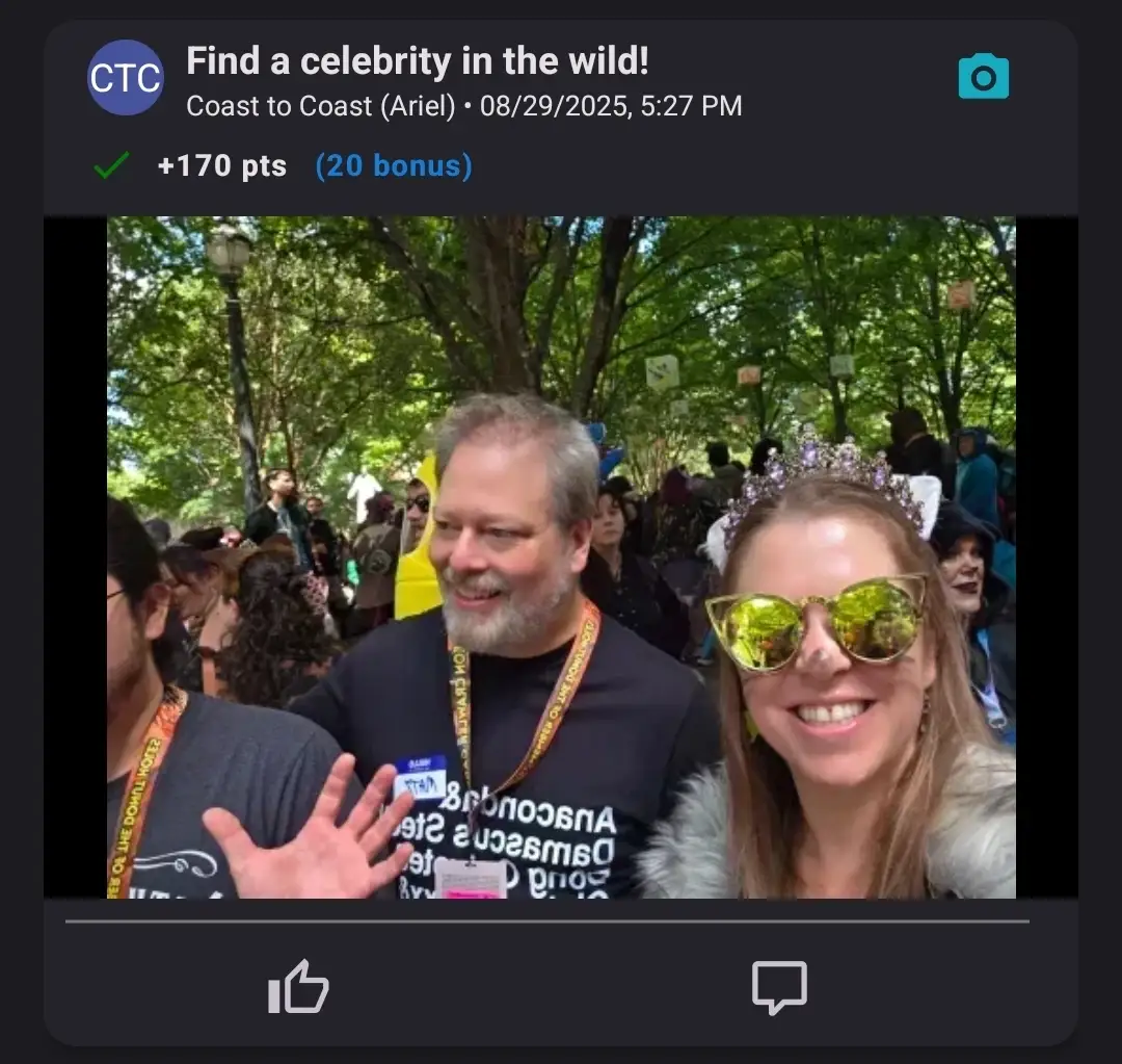 A smiling woman wearing reflective sunglasses posing with a bearded man in a crowd during a celebrity spotting challenge